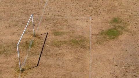 A drought-hit football pitch with goal posts casting a shadow.   