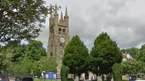 A tall stone medieval church tower with a clock face