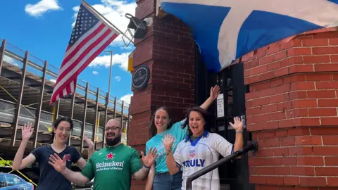 BBC A group of staff wearing football tops on the steps of a bar. Underneath a Scotland flag and a USA flag