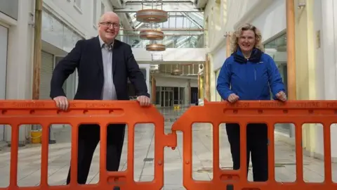 Wychavon District Council A man and woman smile as the stand behind orange barriers in the corridor of a shopping centre.
