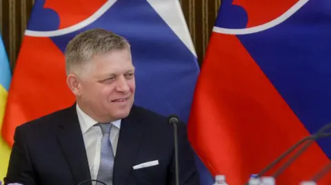 Robert Fico smiling with Slovak flags in background