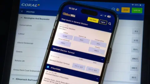Carl Court/Getty Images A phone and a computer screen with betting apps showing odds for political bets ahead of the forthcoming UK general election