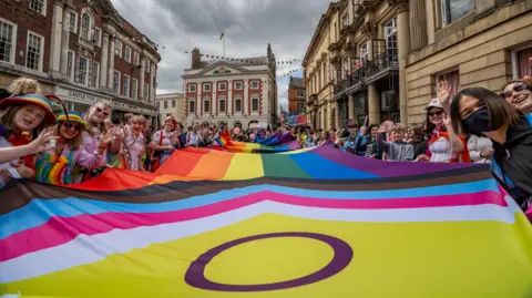 A group of pride supporters holding a giant pride flag outside Mansion House in York.

There are around 20 men, women and children, in the crowd holding onto the flag.