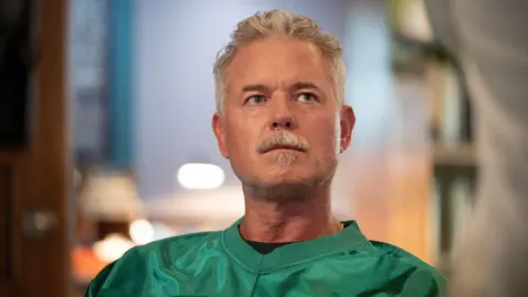 Pief Weyman/NBC via Getty Images A still of Eric Dane in Brilliant Minds. He has short grey hair and facial hair and wears a bright green jersey.