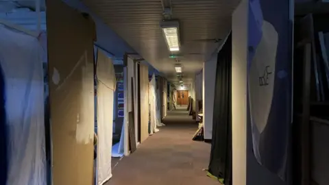 Jenny Kirk/BBC A corridor inside Gildengate House in Anglia Square in Norwich. Fabric is draped from the walls and it is dimly lit by overheat strip LED lighting.