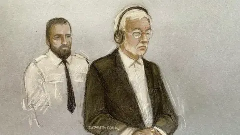 PA A court sketch of Hongchi Xiao today at Winchester Crown Court. He is shown wearing a dark suit jacket and white shirt with no tie, black headphones and glasses. Behind him is a custody officer in a white shirt and dark tie. 