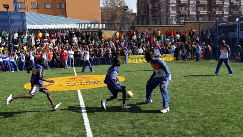 Getty Images Young footballers in action as a large crowd watches on around an artificial five-a-side pitch