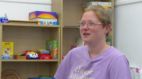 BBC A woman sits in front of shelves full of toys.