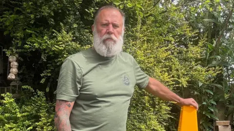 Steve Bonnington Steve Bonnington, in a green t-shirt, standing in front of greenery