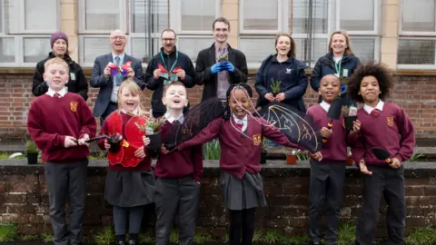Julie Broadfoot A group of schoolchildren standing in front of a group of adults holding plants with excited expressions