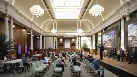 Derbyshire County Council A large hall full of people sat on chairs facing a wooden stage where people are presenting in front of a screen