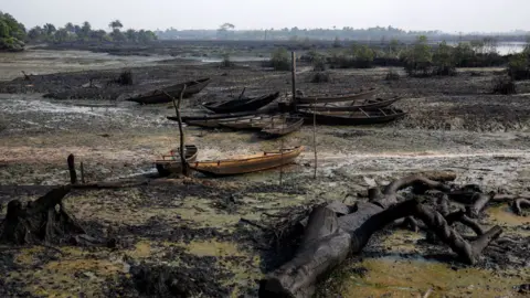Getty Images Abandoned fishing boats sit on the ground as crude oil pollution covers the shoreline of an estuary in the Niger Delta region, Nigeria