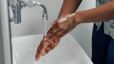 A close up of a persons hands as they wash them under a tap in a sink