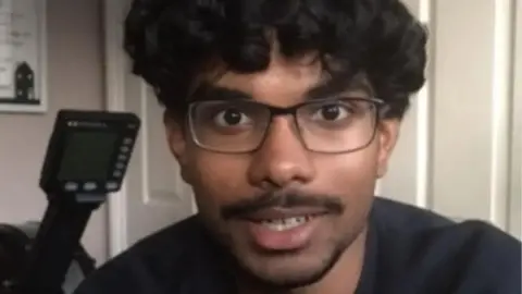 A young man with dark hair and glasses looking at the camera