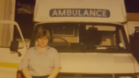 East Midlands Ambulance Service A dated image of Pat Withers, standing in front of an ambulance