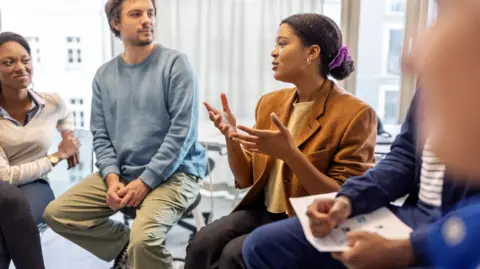 Getty Images A stock shot of a group of people seated, holding a discussion. 