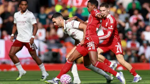 A Liverpool player in all red on the right and an Arsenal 
