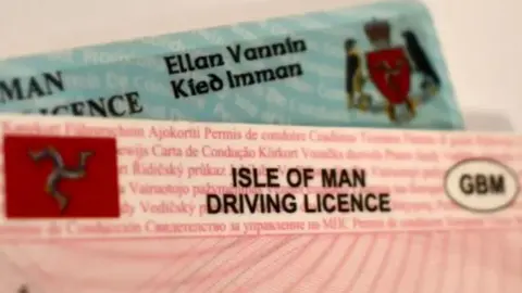 BBC A close-up of two physical Isle of Man driving licences, which are pink and blue.