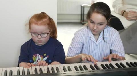 Emmie playing the piano with her sister Evie 
