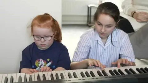 BBC Emmie playing the piano with her sister Evie 