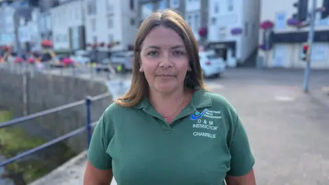 A picture of Chantelle wearing a green polo shirt. She has short brown hair and is stood next to a railing.