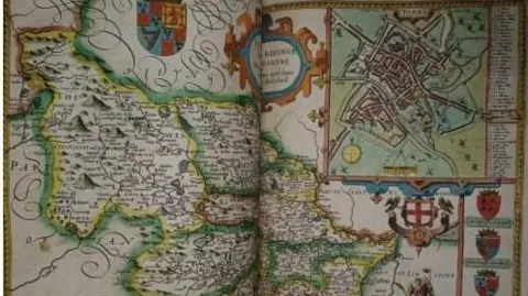 Sheffield Council An old book is open showing a colourful, intricate and detailed map with several family crests and shields