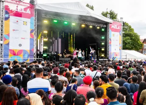 Sandwell Council A crowd watching a musical performance on a large outdoor stage with sponsorship banners either side