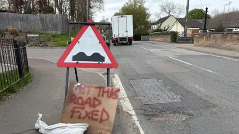 Road with a pothole and a sign calling for the road to be fixed