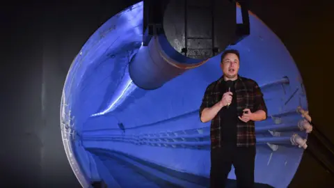Getty Images Elon Musk stood in front of a large tunnel talking to the camera