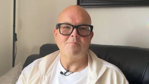 Jody Bunting sitting on a sofa wearing glasses and light coloured clothing