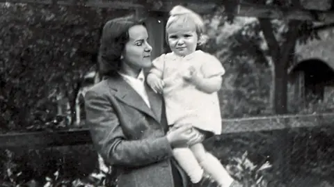 A black and white photo of a woman holding a young child. The woman is wearing late 1940s clothing.