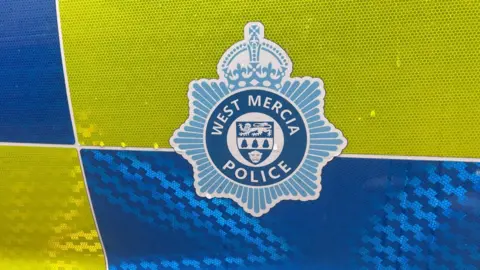 A blue West Mercia Police emblem on the side of a yellow and blue police vehicle.