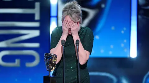 Getty Images Evans on stage accepting her award. Her hands cover her face