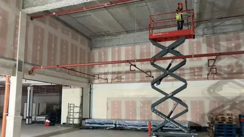 A man on mobile elevated work platform looking down at an empty shop unit which has been stripped back and is under construction.