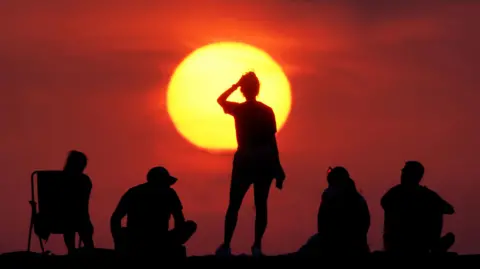 Five people stare at a glowing yellow sun at sunset.