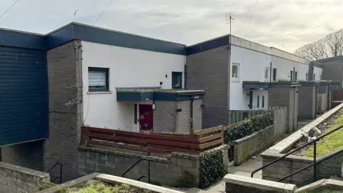 Row of buildings in Aberdeen, with fencing, paths and steps visible, under a cloudy sky.