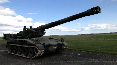 Royal Artillery Museum The long barrel of a self-propelled howitzer set against the rolling Wiltshire countryside.