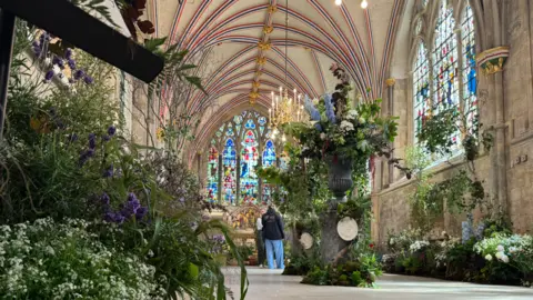 George Carden/BBC One of the rooms in the cathedral filled with green and colourful plants, in the background is a stainglass window and colourful patterns that go up the ceiling