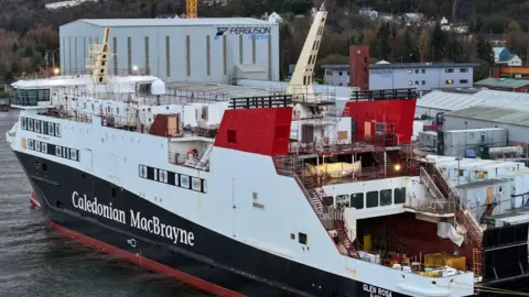 Getty Images A black and white ship with red funnels, moored in front of a later fabrication shed. 