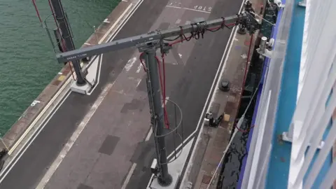A crane stands in the docks with plug in cables attached.