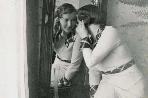 The General Elżbieta Foundation, Toruń Posed black and white photo of Zo looking into a mirror while wearing a white dress with decorative cuffs and belt