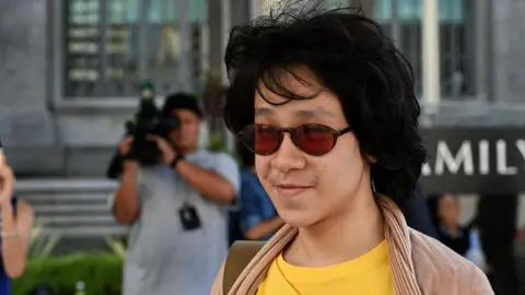 Amos Yee, in a yellow t-shirt and brown sunglasses, arrives at the state court in Singapore on June 2, 2015