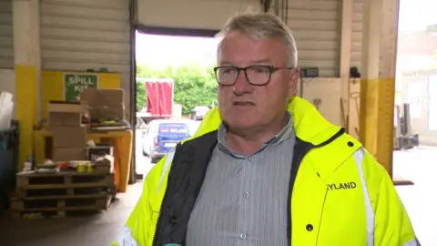 Hyland Shipping Hyland Shipping's managing director Tino Hyland talks to the BBC wearing a fluorescent jacket over a shirt