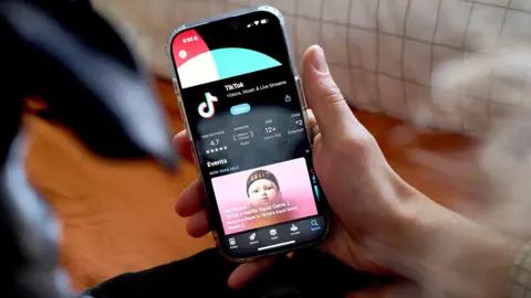 Getty Images Photograph of a hand holding an iphone, which has the Tiktok app download screen on it. 