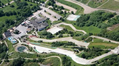 Supplied Aerial shot of outdoor dry ski slopes surrounded by grass and trees.