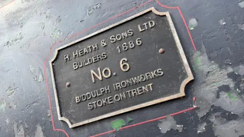 A name plate on the side of a steam locomotive, which indicates it was built in 1886 and based at Biddulph Ironworks. The paintwork around the nameplate is crumbling.