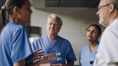 Getty Images Two men and two women standing in a circle wearing medical scrubs. Stock Image