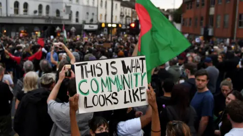 anti-racism protestors gathered in Walthamstow  - one holding a placard saying "this is what community looks like"