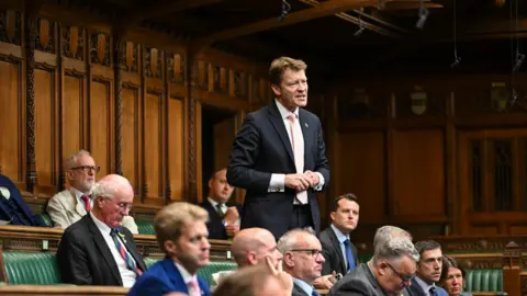 House of Commons Man in suit stood in house of commons speaking surrounded by other men
