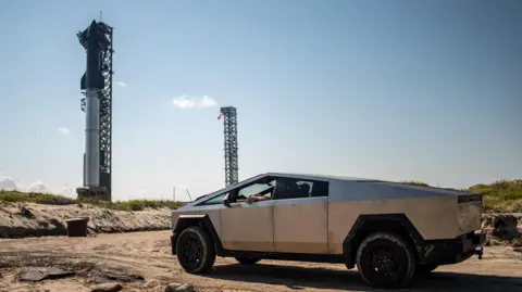 Sergio Flores/AFP/Getty Images A Tesla Cybertruck menghadapi kapal luar angkasa SpaceX saat duduk di landasan peluncuran di Starbase dekat Boca Chica, Texas, pada 12 Oktober 2024, menjelang tes Starship Flight 5. 